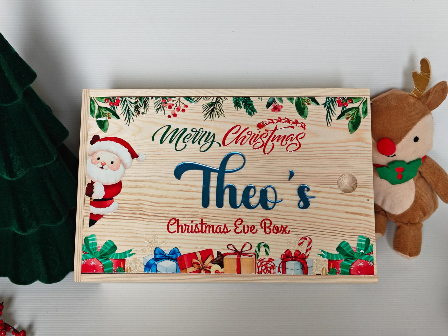 Wooden Christmas Eve box with festive design and 'Theo's Christmas Eve Box' text, surrounded by Christmas decorations.