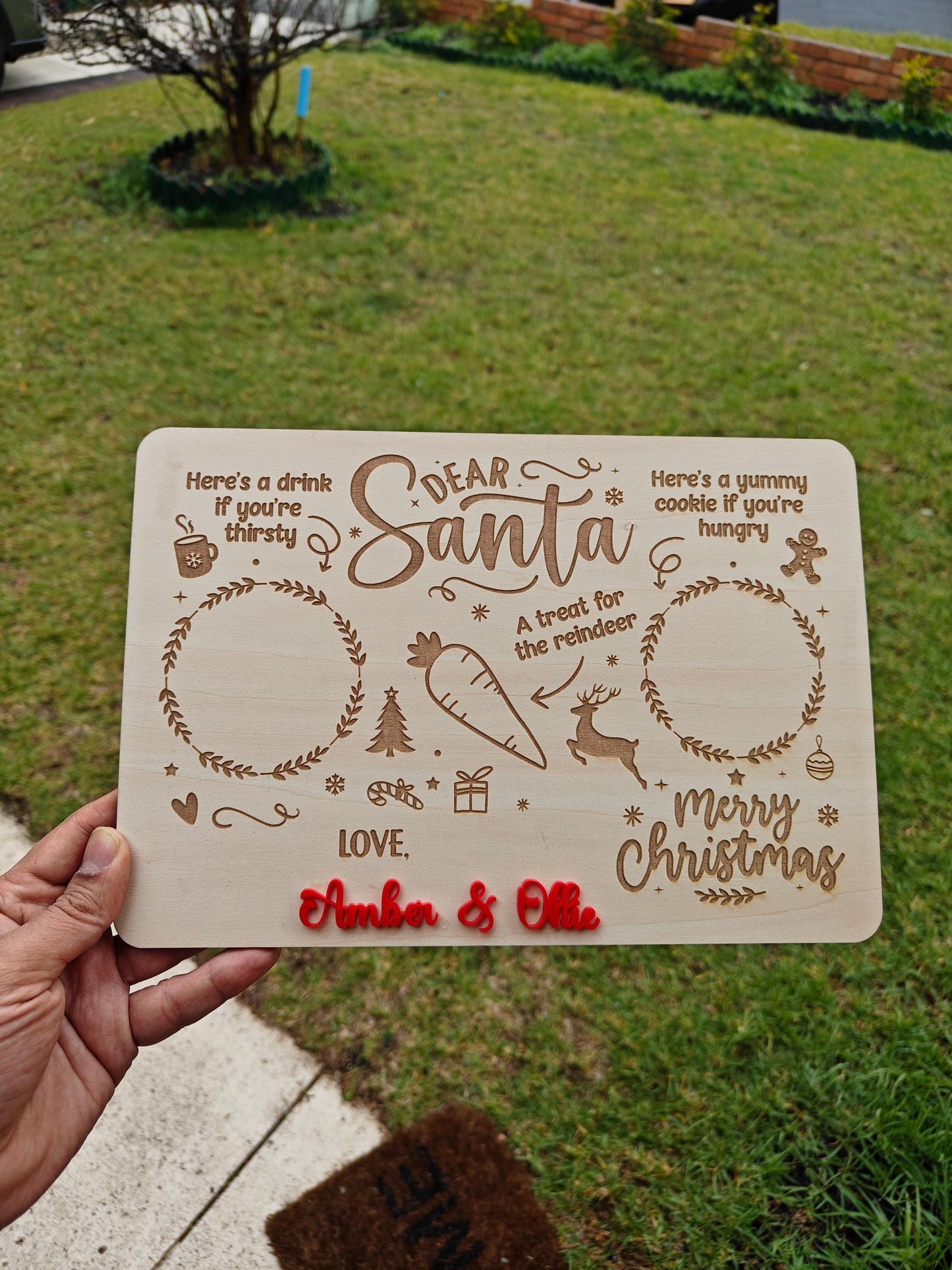 Decorative sign with Christmas-themed text held outdoors on a grassy background