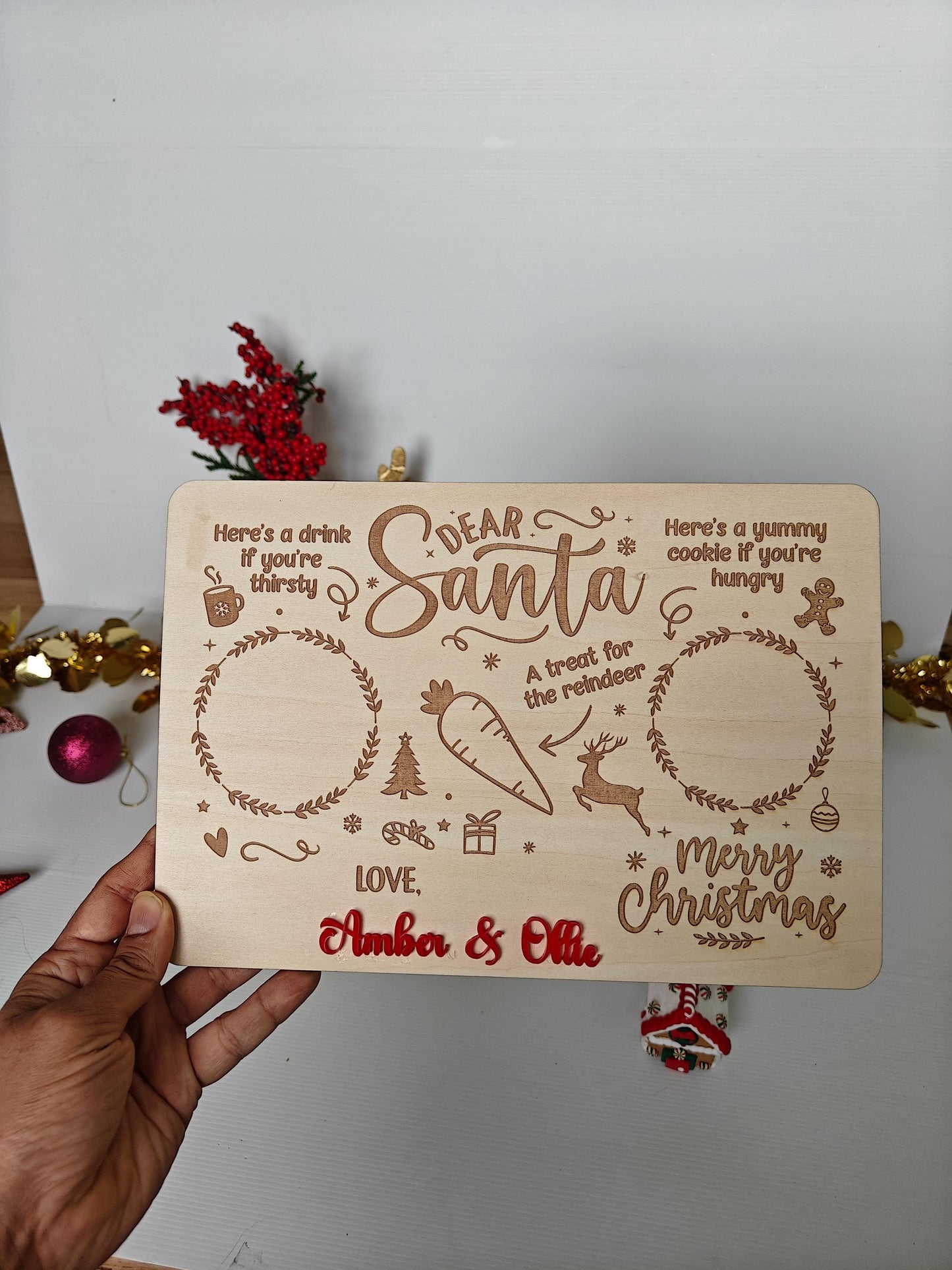 Wooden Christmas card with decorative text and illustrations held by a hand against a white background.